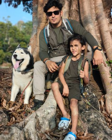 Super host Bajan Bopanna and Viaan (The Indian Mowgli) sitting with Whisky the husky under a large tree at Evergreen County, Coorg