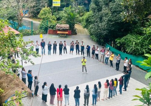 A group of professionals standing in a large circle during an outdoor leadership workshop at a nature resort.