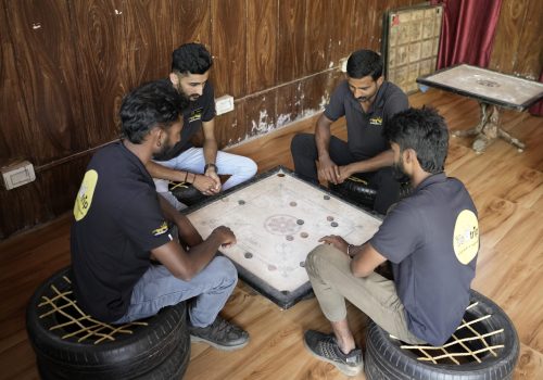 Guests playing carrom in the indoor activities area at Evergreen County Resort, a premier adventure and pure veg resort in Coorg.