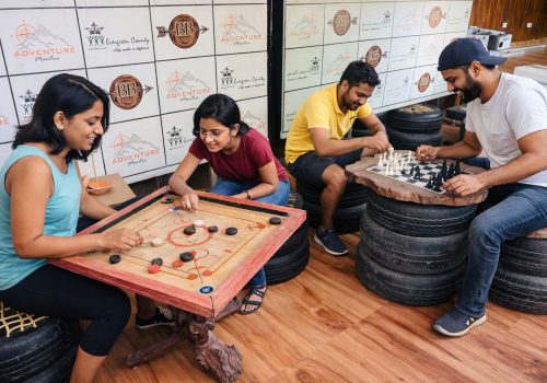 Guests enjoying carrom and chess on rustic eco-friendly furniture at Evergreen County's indoor activity center.